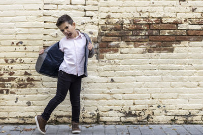 Full length portrait of boy shouting while standing against brick wall