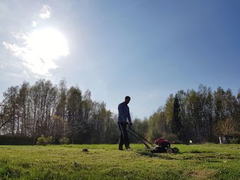 Man cleaning field with lawn mower against sky