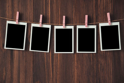 Close-up of blank instant print transfers hanging with clothespins on string against wooden wall