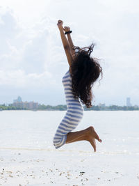 Woman jumping at beach against sky