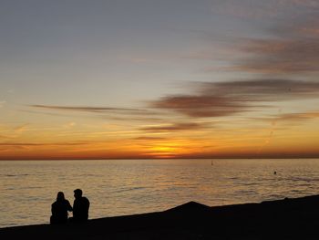 Silhouette people looking at sea against sky during sunset