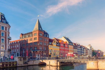 Nyhavn bridge across a canal with old ships, colorful houses and old  church in copenhagen, denmark