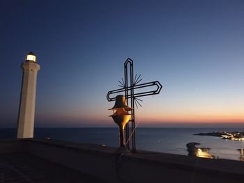 Lighthouse by sea against clear sky during sunset