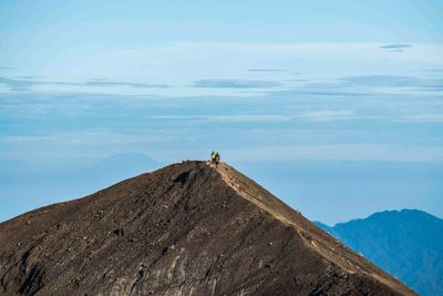 People hiking on top of mountain against cloudy sky