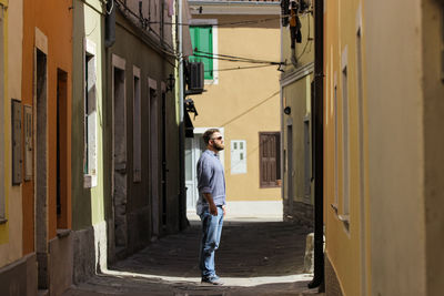 Man standing on alley amidst buildings in city