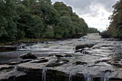 Scenic view of waterfall in forest against sky