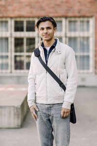 Portrait of smiling teenage male student standing with crossbody bag in high school campus