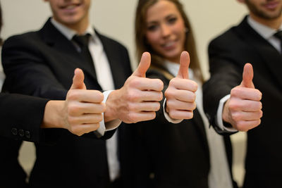 Midsection of business people showing thumbs up while standing in office