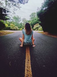 Rear view of woman sitting on road against trees