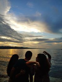 Friends at beach against sky during sunset