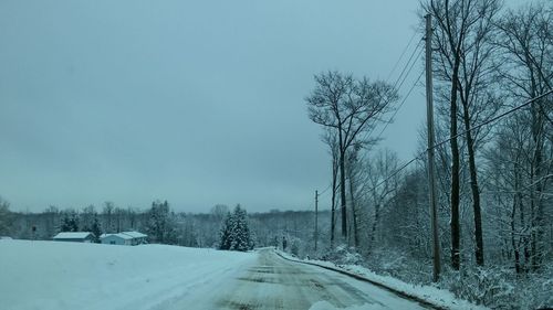 Road amidst snow covered land and trees against sky