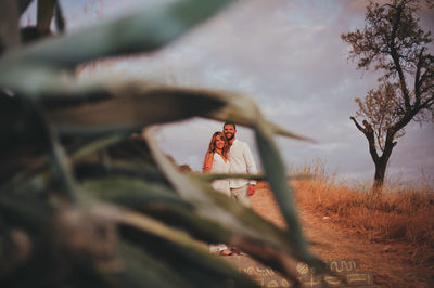 Portrait of young couple standing on steps seen through plant