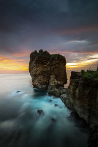 Rock formation in sea against sky during sunset