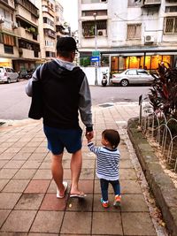 Rear view of father and son walking on street in city
