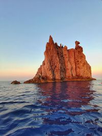 Rock formations in sea against clear blue sky