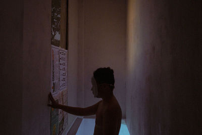 Side view of man standing against wall at home