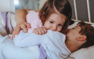 Cheerful sister biting brother on shoulder while lying on bed at home