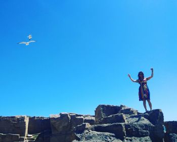 Low angle view of helicopter flying over rocks against clear blue sky