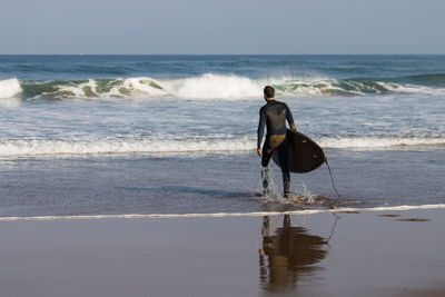 Rear view of man with surfboard walking on beach