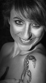 Close-up portrait of beautiful smiling young woman with tattoo against black background