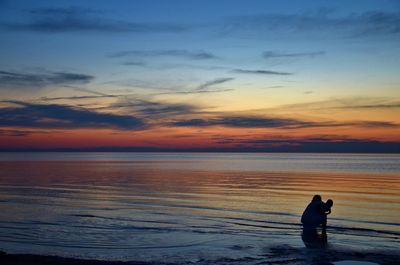 Silhouette mother and child enjoying at beach against sky at dusk