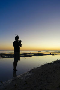 Silhouette man standing at beach against clear sky during sunset