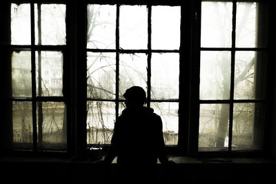 Silhouette person looking through window