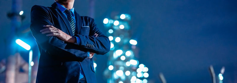 Midsection of man standing against illuminated blue wall at night