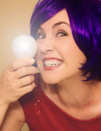 Close-up portrait of smiling young woman holding light bulb