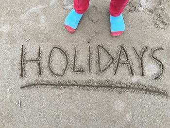 Low section of boy with text on sand at beach
