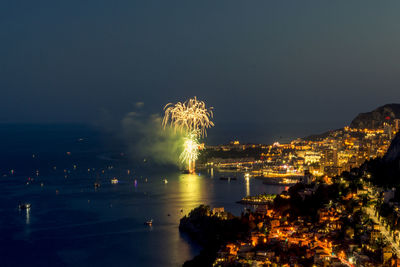 Firework display over sea against sky at night