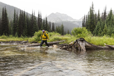 Tourist with backpack crossing river in highland area on cloudy day