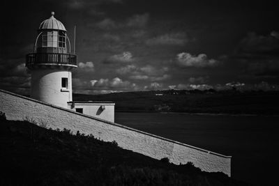 Lighthouse by sea and buildings against sky