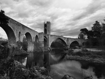 Low angle view of romanesque bridge over river against cloudy sky