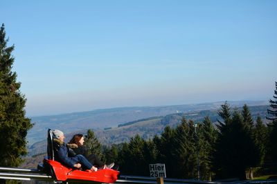 Woman sitting on mountain against blue sky