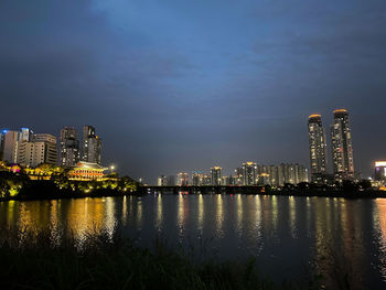 Illuminated city by river against sky at night