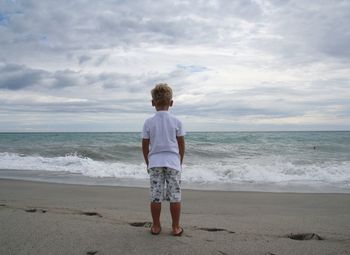 Rear view of boy standing on beach against sky