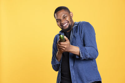 Young man using mobile phone while standing against yellow background