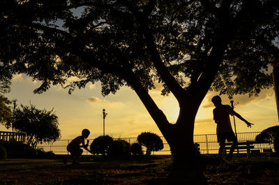 Silhouette people playing on field against sky during sunset