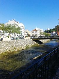 Buildings by river against clear blue sky