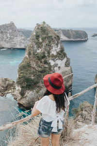 Rear view of woman standing on rock by sea