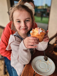 Portrait of smiling girl eating cupcake sitting at restaurant with mother