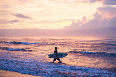 Surfer on beach against sky during sunset