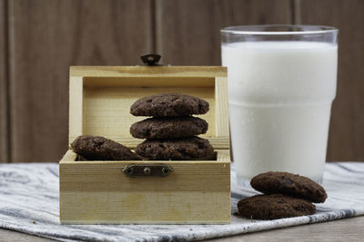 Dark chocolate cookies inside the treasury box and a glass of milk over wooden background. 