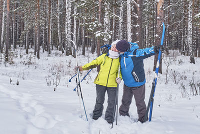 Happy mature couple in winter sportswear with cross-country skis kissing in snowy forest