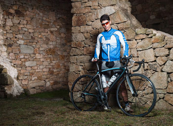 Full length of man with bicycle standing against stone wall