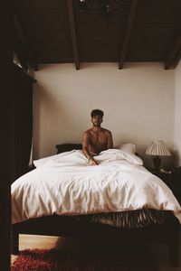 Portrait of shirtless young man sitting on bed