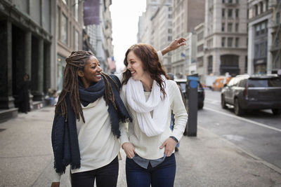 Female friends smiling and enjoying while standing on footpath