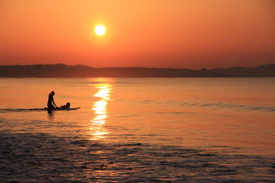 Silhouette person in sea against sky during sunset