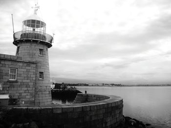 Lighthouse on sea against cloudy sky